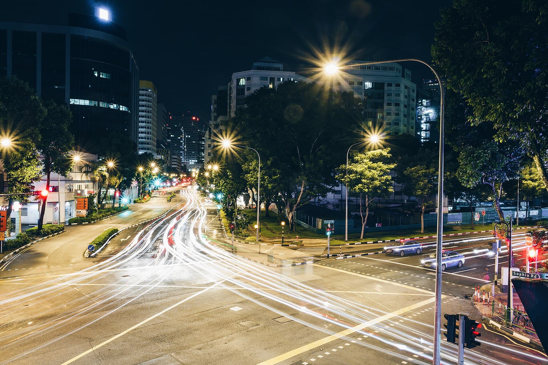 Cruce urbano de noche con estelas de luz de autos en movimiento