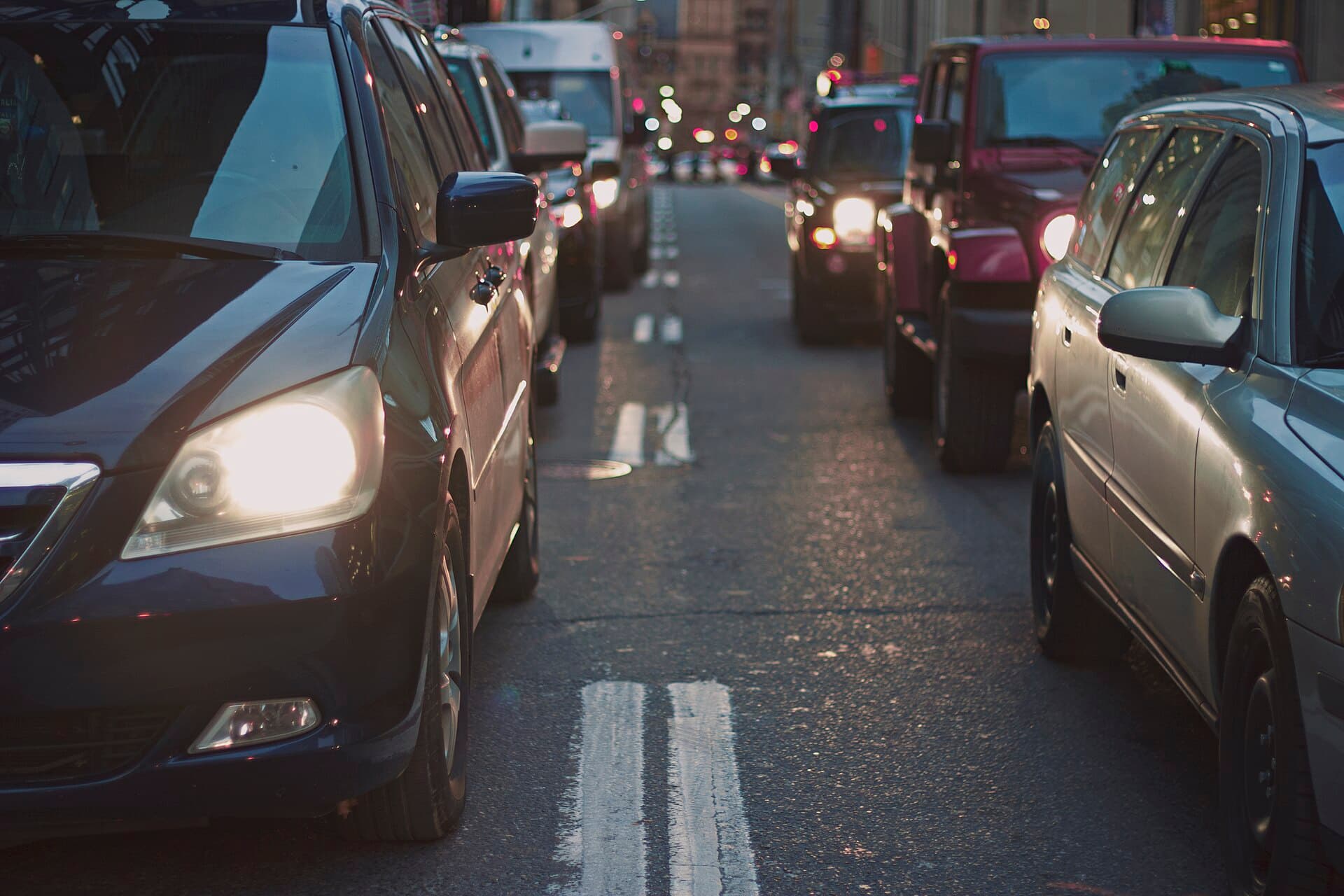 Fila de autos con las luces encendidas en una avenida al atardecer